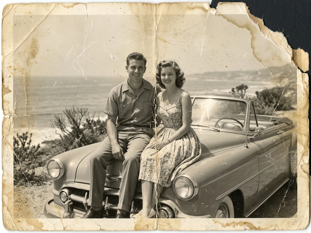 A faded, creased black-and-white print of a couple sitting on a vintage car